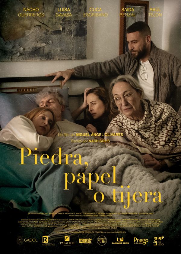 Pòster del curtmetratge 'Piedra, papel o tijera'. Mostra tres dones i dos homes a sobre d'un llit, vestits amb roba informal. Un home gran i una dona jove es veuen estirats al llit, un home amb barba i dues dones grans se'ls miren. El títol, 'Piedra, papel o tijera', està escrit en lletres grans a la part inferior. Els noms dels actors principals, com ara Nacho Guerreros i Luisa Gavasa, es troben a la part superior.